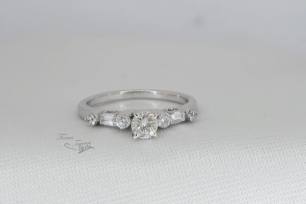 Anillo con diamante central
redondo de 23 pts,  2 redondos y un canutillo a cada lado 24pts laterales